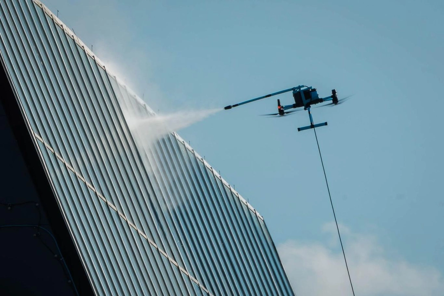 Break Facility Service - Eine Drohne besprüht die Glasfassade eines Wolkenkratzers mit Wasser.